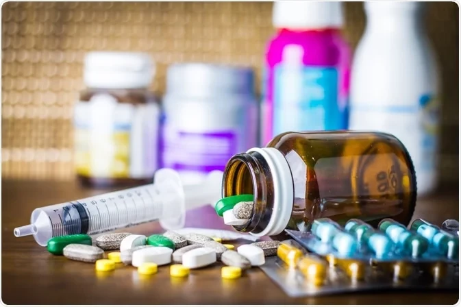 A tipped brown medicine bottle beside a syringe and assorted pills and blister packs on a table.