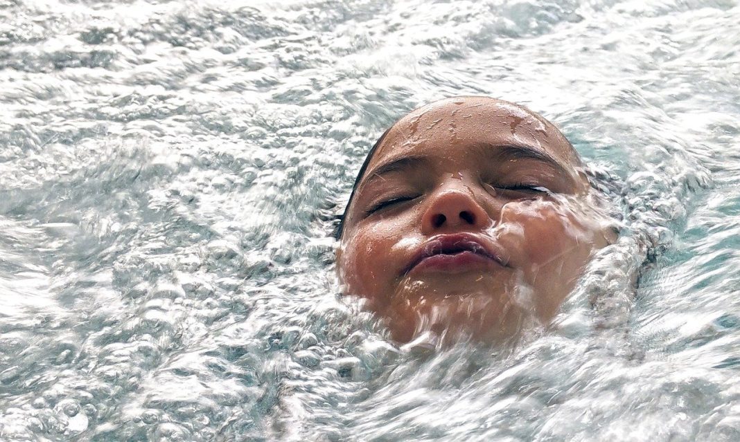 Close-up of a child floating on their back in churning water, with splashes around their face.
