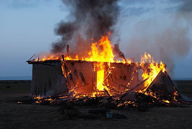 A small hut burns intensely at night, with flames and thick smoke rising into the sky.