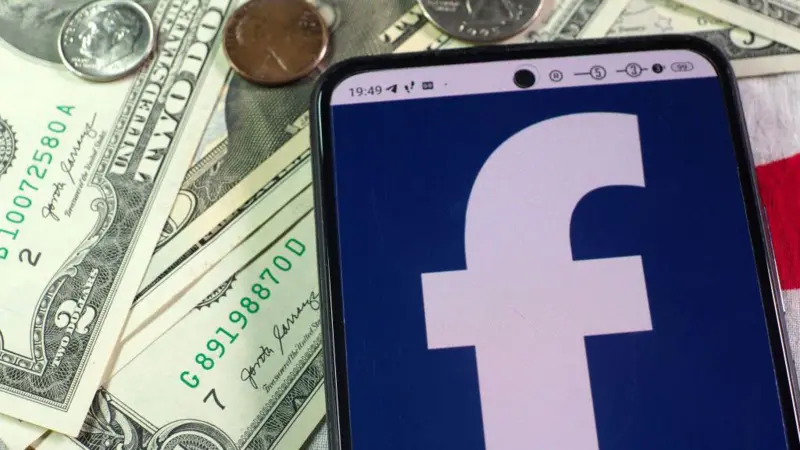 Smartphone showing the Facebook logo placed on US dollar banknotes and coins.