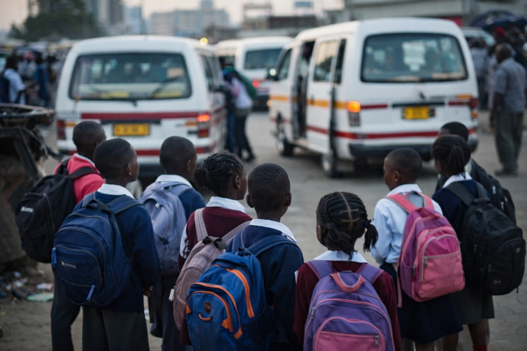 Schoolchildren with backpacks waiting near commuter omnibuses in Harare after transport fares increased