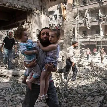 A man carries two children through rubble after destruction in a war-affected urban area in the Middle East