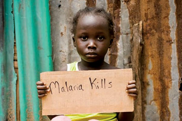 A young child holds a cardboard sign reading “Malaria Kills” as malaria deaths rise in Mashonaland Central.