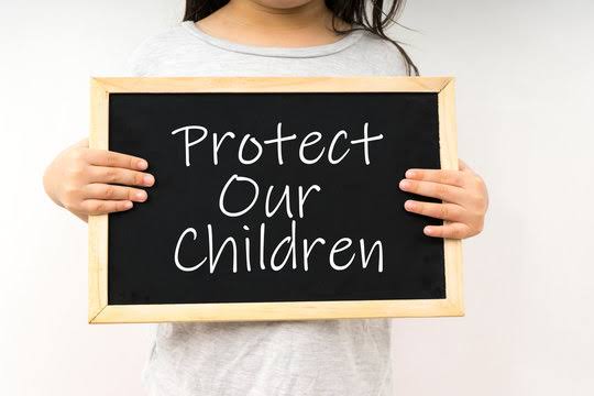 Child holding a chalkboard with the words “Protect Our Children.”